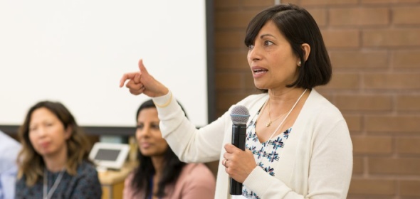 Photo of Dr. Sunita Mutha speaking with a microphone at a large meeting.