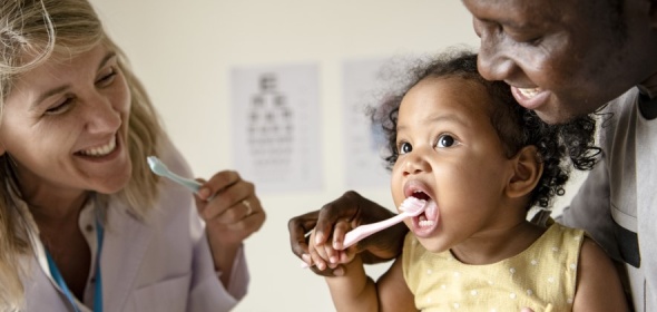 Photo of toddler using a toothbrush with mother and dentist