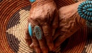Stock photo of elderly woman's hands with turquoise and silver jewelry resting on an intricate woven basket.