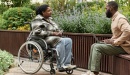 Photo of woman in wheelchair talking to man seated with laptop in an outdoor courtyard